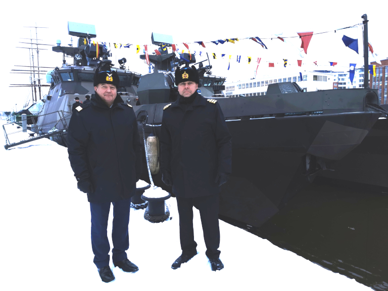 Kaksi univormupukuista sotilasta lumisella laiturilla ohjusveneen edessä