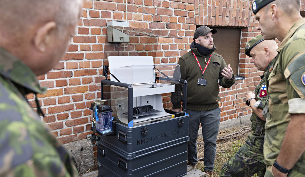 Kuvassa neljä miestä, kolme sotilasta ja yksi siviili, tutustuvat 3d-tulostimeen.