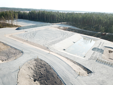 - the open, wide area of Syndalen’s new explosion site which consists of an explosion field, water treatment pool and a protection berm made out of crushed stone.  Forest in the background.