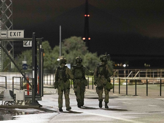 Military police are performing a security duty in an urban area: three conscripts are moving around outdoors in the dark in combat gear.