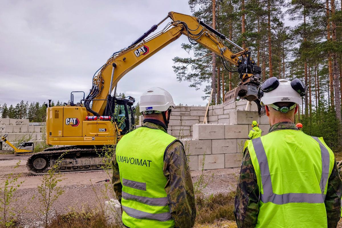Rakennusmiehiä ja kaivinkone rakentamassa betonilinnoitetta