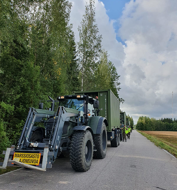 Jono perävaunua vetäviä liikennetraktoreita pysähtyneenä tien varteen.