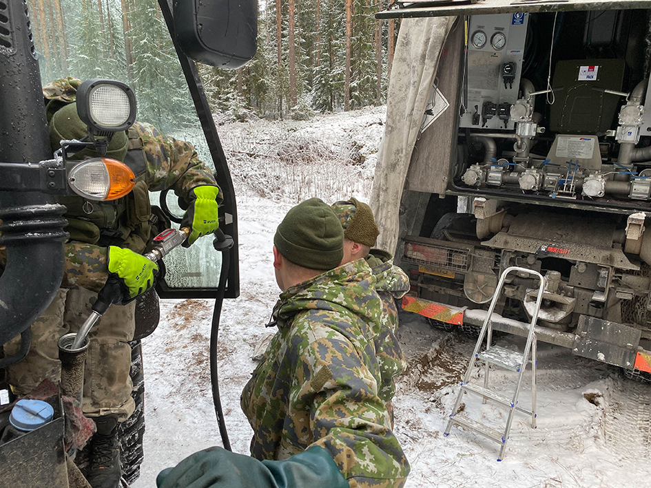 Maastopukuiset sotilaat tankkaavat ajoneuvoa säiliöautosta lumisessa maastossa.