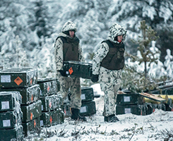 Kaksi sotilasta kantaa ammuslaatikkoa talvisessa maastossa. Kuva Puolustusvoimat.