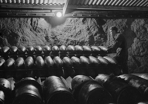 In this photograph in black and white from 1944, a soldier is examining artillery munitions arranged in line in a depot. Photo by Finnish Defence Forces. Photo by Finnish Wartime Photograph Archive SA-kuva.