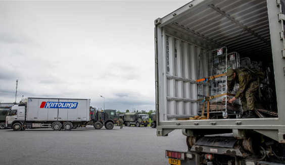Trucks at the logistics centre. A soldier wearing a combat uniform is attaching a trolley in a truck’s cargo space. Photo by Finnish Defence Forces.