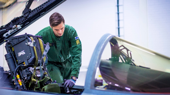 Vihreään haalariin pukeutunut mekaanikko tutkii Hornet-hävittäjän ohjaamoa. Kuva Puolustusvoimat.
