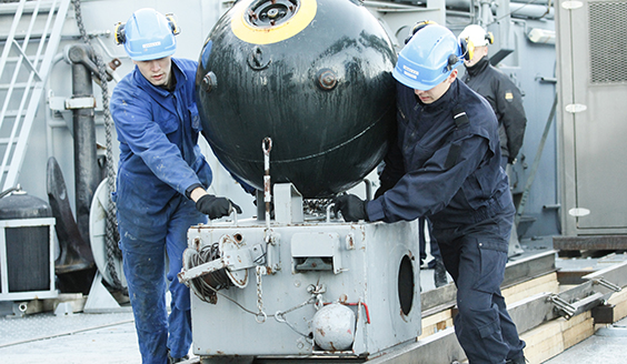 Two navy soldiers in overalls are moving a sea mine on the deck. Photo by Finnish Defence Forces.